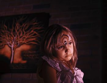 Girl with face paint looking away against wall