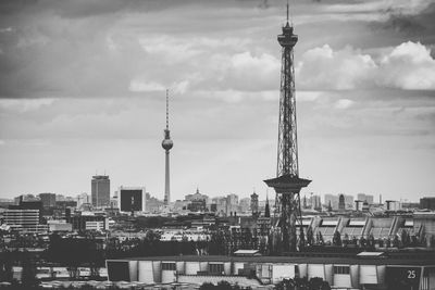 Communications tower in city against cloudy sky