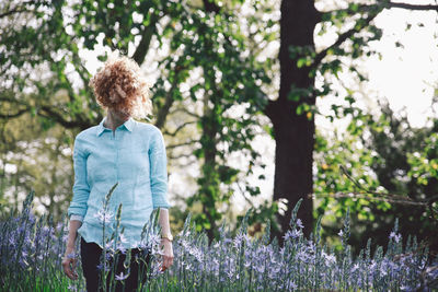 Woman standing amidst purple flowering plants at forest