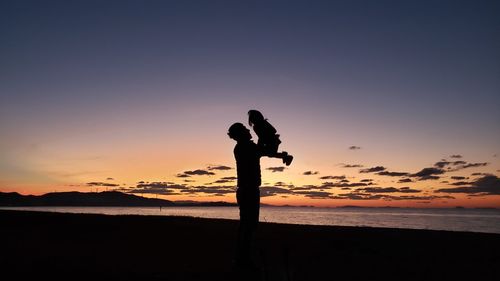 Silhouette woman standing on beach against sky during sunset