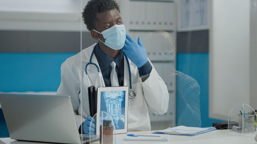 Doctor using digital tablet while working in laboratory with reflection of woman