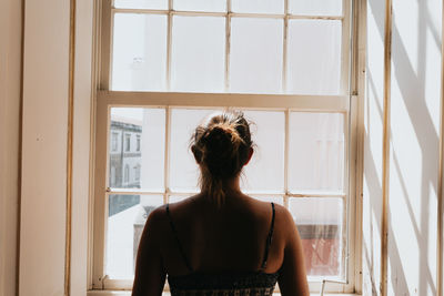 Portrait of young woman standing against window