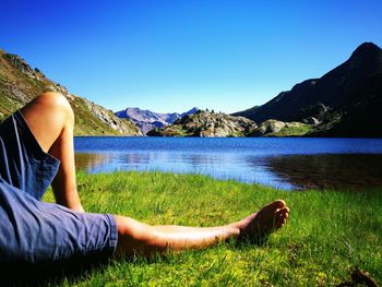 Low section of woman relaxing on grass by lake against sky