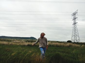 Smiling woman standing on field against electricity pylon