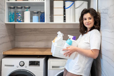 Portrait of smiling young woman drinking water while standing at home