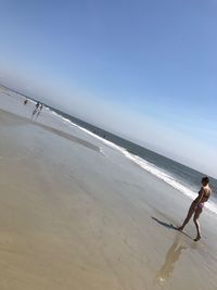 Tilt shot of woman walking on beach against clear sky