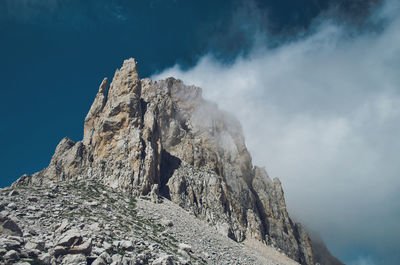 Low angle view of rocky mountains against cloudy sky