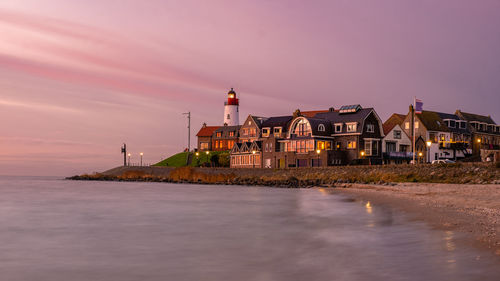 Lighthouse by sea against sky at sunset