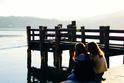 Rear view of women sitting on pier at lake