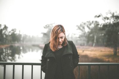 Young woman standing by railing against sky during winter