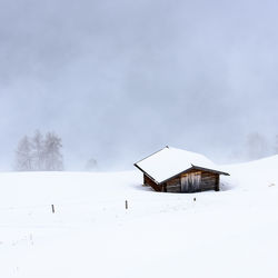 House on snow covered landscape against sky