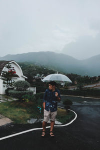 Woman standing on wet road against sky during rainy season