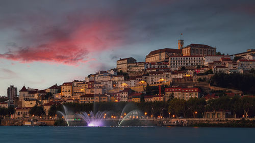 Illuminated buildings in city against cloudy sky