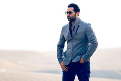 Handsome young man standing on sand at desert against clear sky