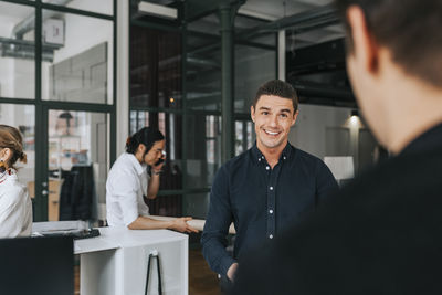 Smiling businessman looking at male colleague at office