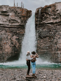 Full length of friends standing on rock in front of waterfall at crescent falls, alberta