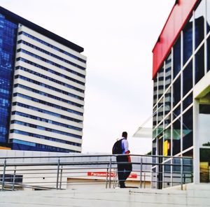 Rear view of man standing by railing against buildings in city