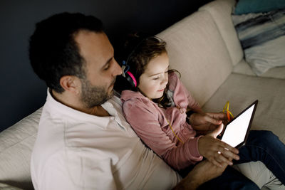 High angle view of father assisting daughter in using digital tablet on couch at home