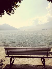 Empty bench by sea against sky