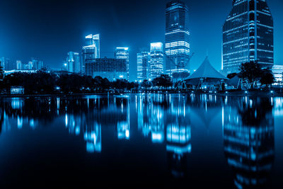 Illuminated buildings by lake against sky in city at night