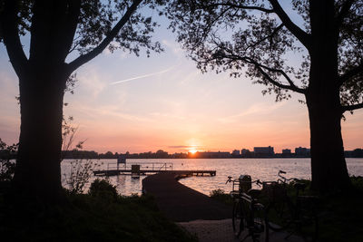 Silhouette tree by river against sky during sunset