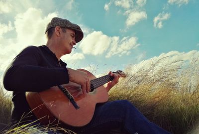 Man playing guitar on field against sky