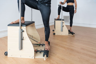 Side view of unrecognizable sportspeople balancing on pilates chairs while doing exercises during workout in bright gym