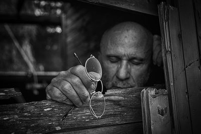 Close-up of thoughtful man with eyeglasses by wooden window