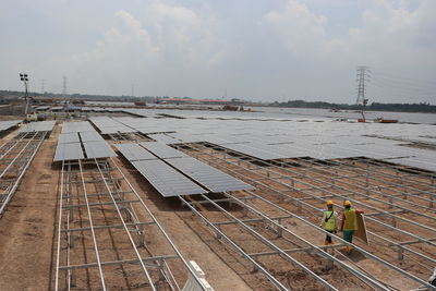 Engineers adjusting solar panels against sky