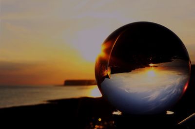 Close-up of crystal ball against sea during sunset