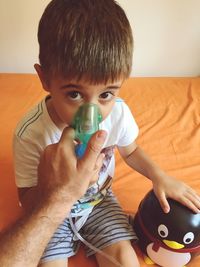 Cropped hand of father holding oxygen mask for son on bed