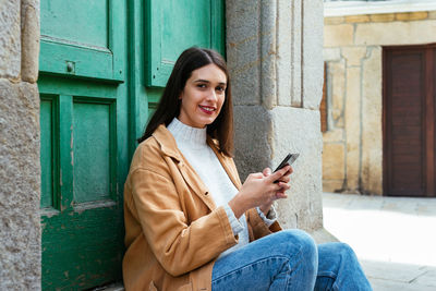 Young woman using mobile phone while sitting in city