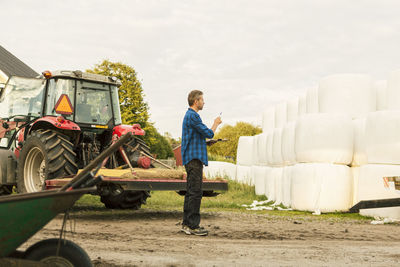 Farmer analyzing covered hay bales while standing by tractor at farm