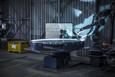 Welder standing behind industrial lathe cutting steel in factory