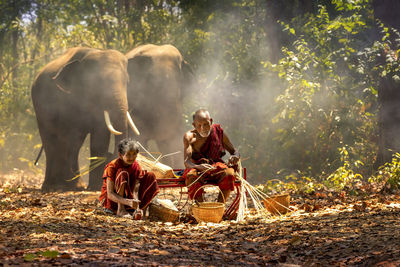 Couple making wicker baskets with elephants in forest