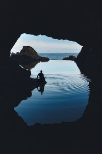 Silhouette person on rock by sea against sky