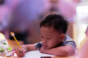 Cute boy writing in book while sitting at table