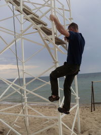 Mid adult man climbing on metallic structure of lookout tower at beach