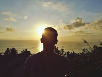 Rear view of silhouette woman standing at beach during sunset