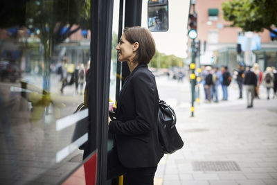 Side view of smiling businesswoman boarding bus in city