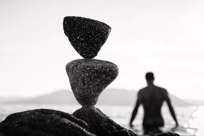 Close-up of stacked rocks at beach against man standing in sea