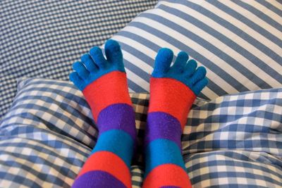 Low section of person wearing colorful socks on bed