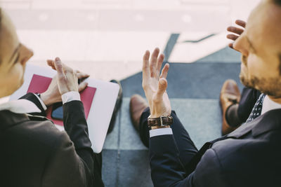 High angle view of businessman talking to coworker while sitting on staircase in city