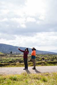 Rear view of friends standing on landscape against cloudy sky