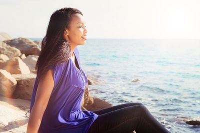 Beautiful young woman looking away at sea shore against sky