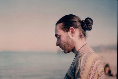 Side view of young man looking down while standing against sea