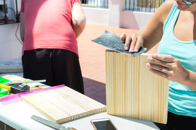 Woman sanding a piece of wood to build a shelf with her partner.