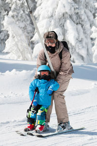 Mature woman teaching son skiing on snow covered field