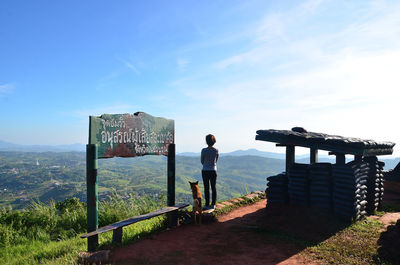 Rear view of woman standing on mountain against blue sky