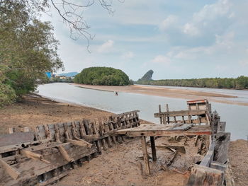 Empty chairs and table by lake against sky